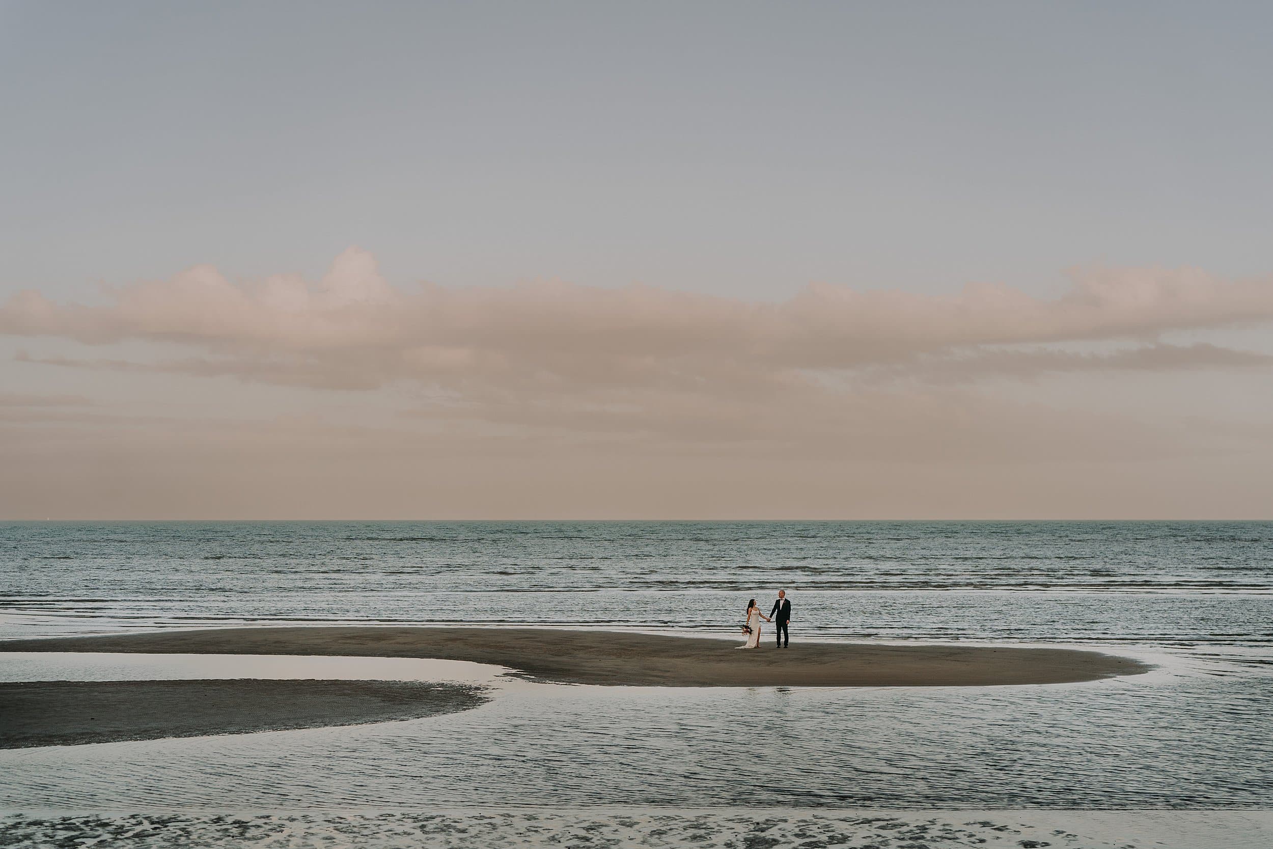 Extreme wide angle wedding photo of bride and groom on island of sand at sunset